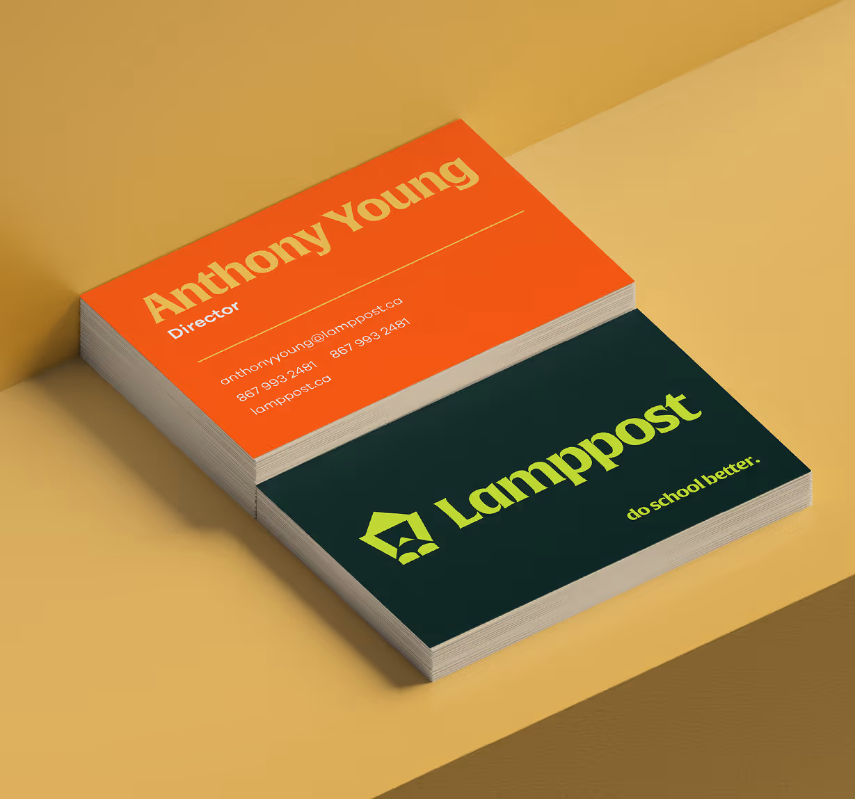 Stack of business cards with one showing Anthony Young, Director, with contact details on an orange background, and the other showing the Lamppost logo and slogan 'do school better.' on a dark green background.