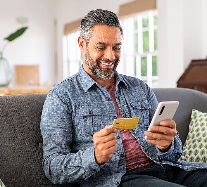 man sitting on couch looking at his phone and credit card