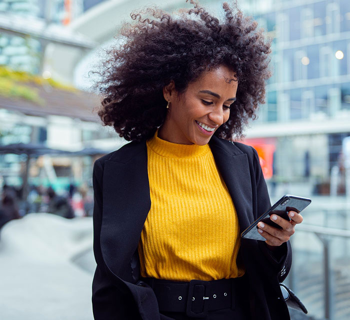 woman walking down the street, looking at her phone and smiling