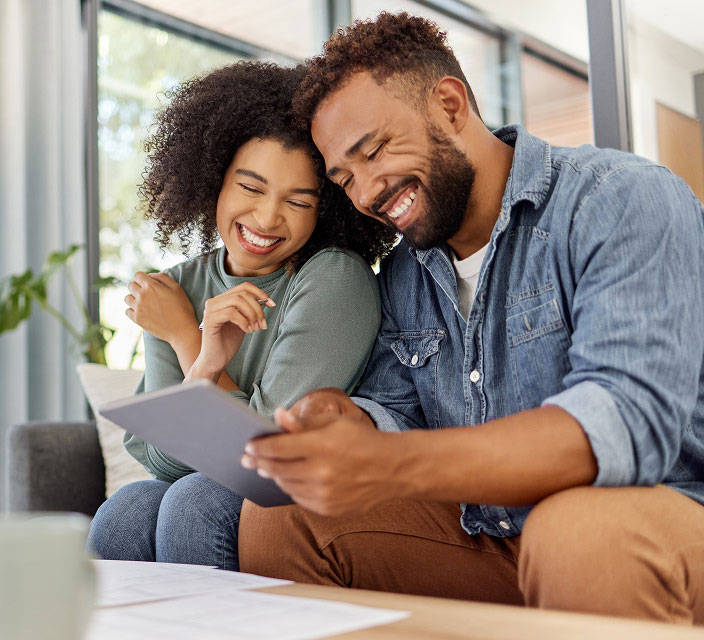 woman and man sitting on couch, smiling, looking at a tablet