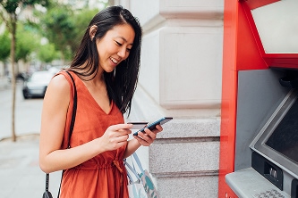 woman looking at her phone while standing at an ATM