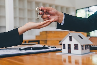 close shot of person handing keys to another person over a table with documents and a small model home