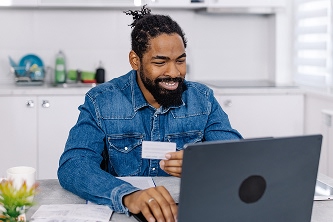 man sitting at a table looking at a laptop and holding a credit card