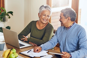 woman and man sitting at a table and smiling while looking at documents and laptop