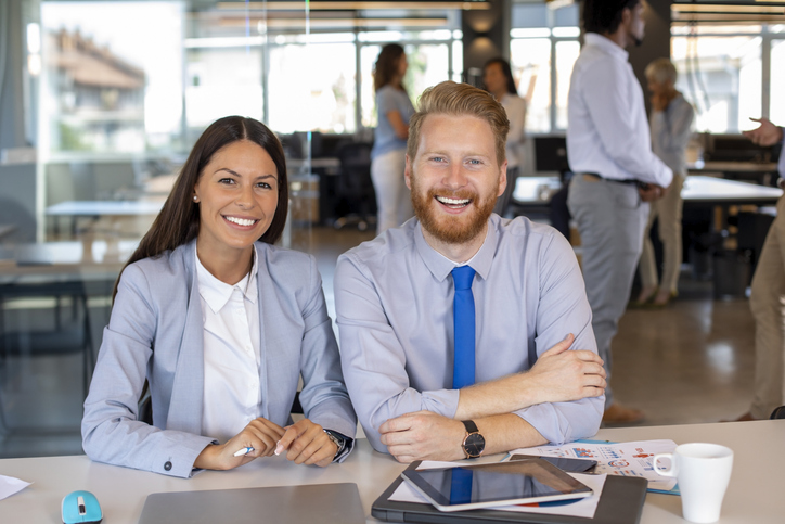woman and man in business attire sitting at a desk smiling 
