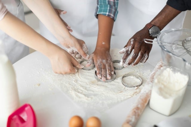 Hands kneading dough together on a floured surface with baking ingredients