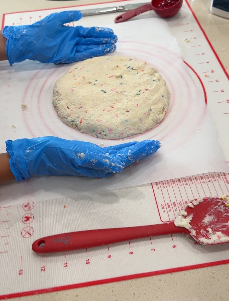 Hands in blue gloves preparing funfetti cookie dough on baking mat