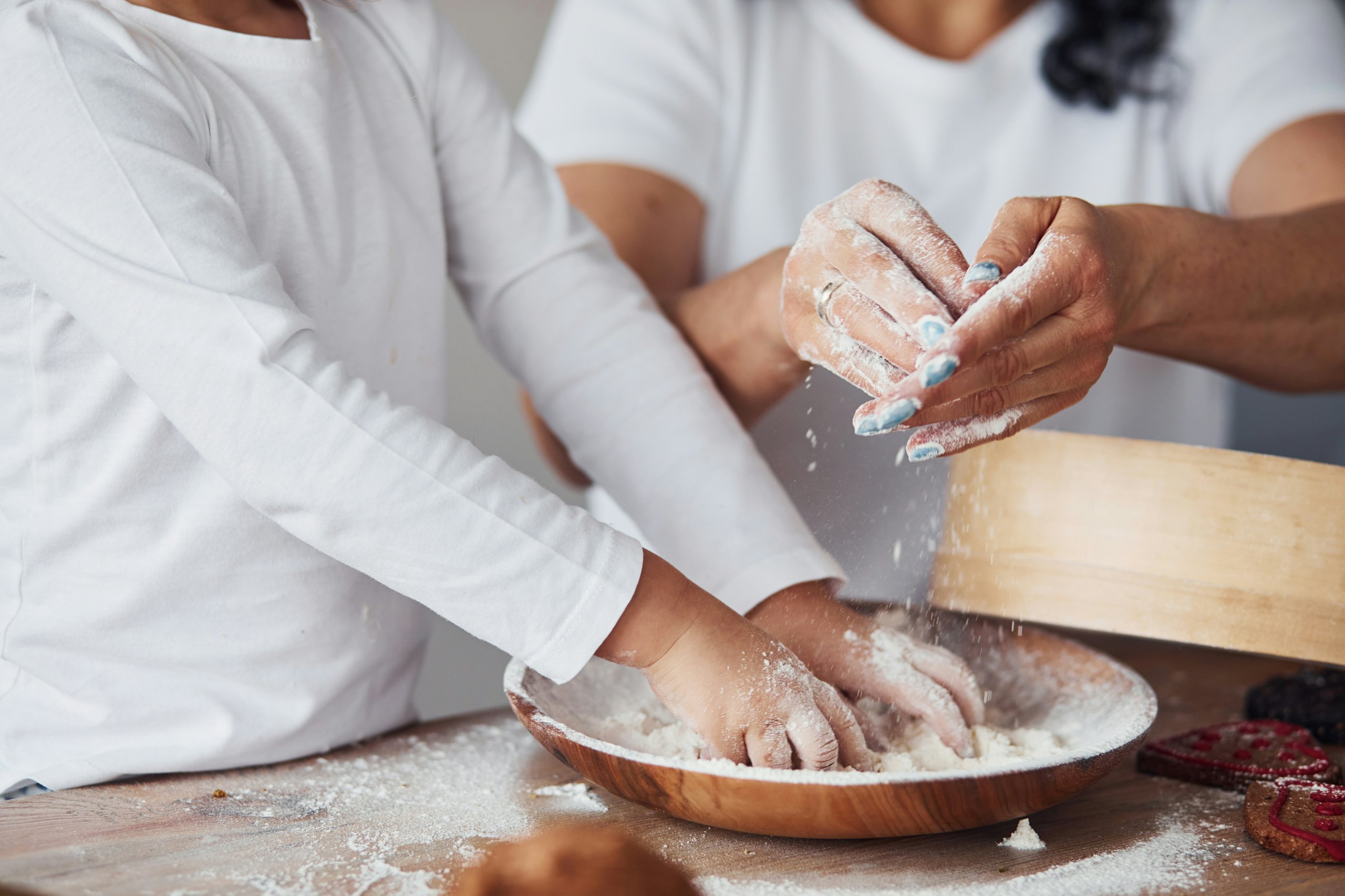 Hands covered in flour kneading dough in a wooden bowl