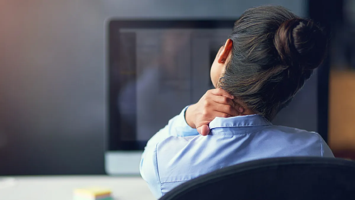 Employee with neck pain at her computer, representing workforce health risks that wellbeing data may fail to reveal