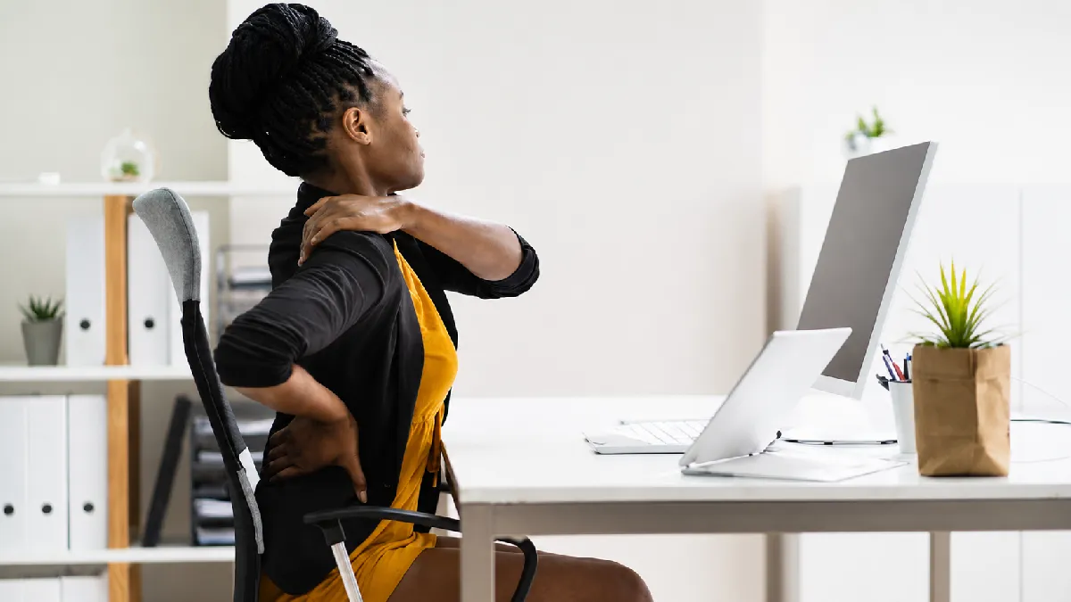 Employee experiencing neck and back pain at her desk, highlighting the need for prevention in workforce health strategies