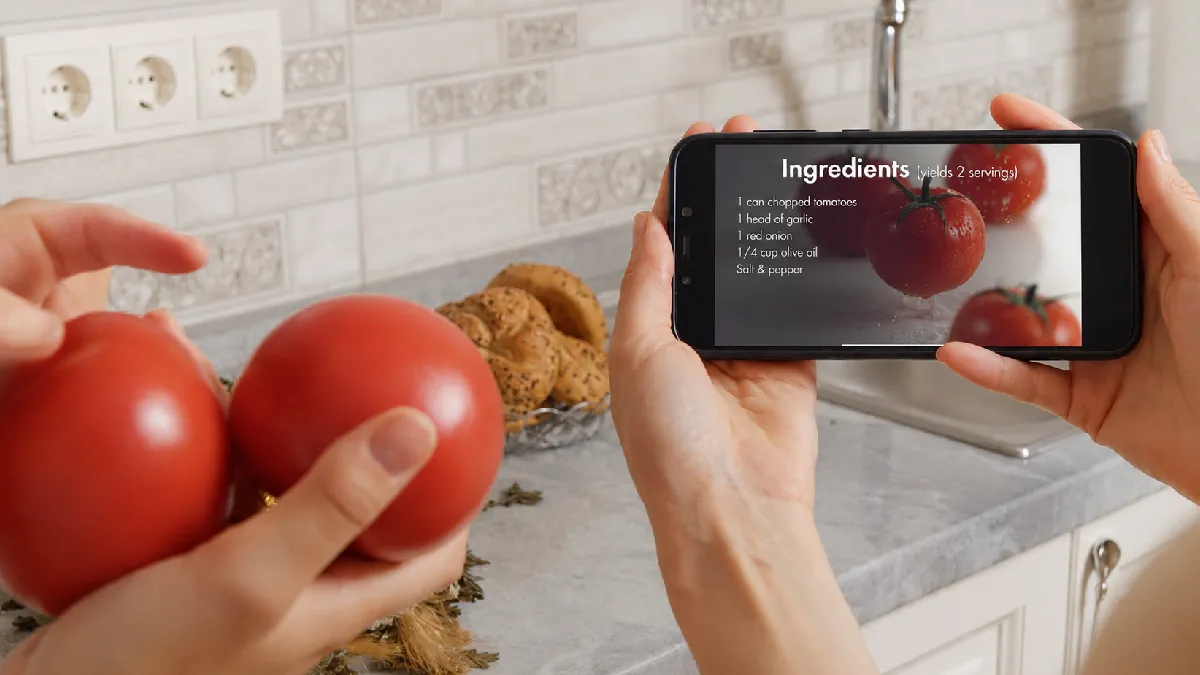 Person using a wellbeing app to view healthy recipe ingredients while preparing tomatoes at home
