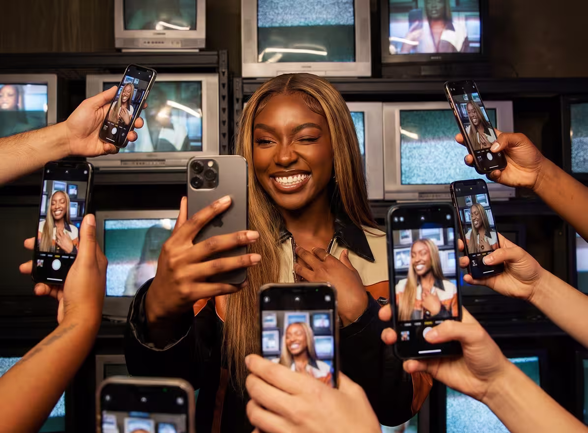 Junge Frau macht Selfie, umgeben von mehreren Smartphones, die Bilder von ihr aufnehmen.