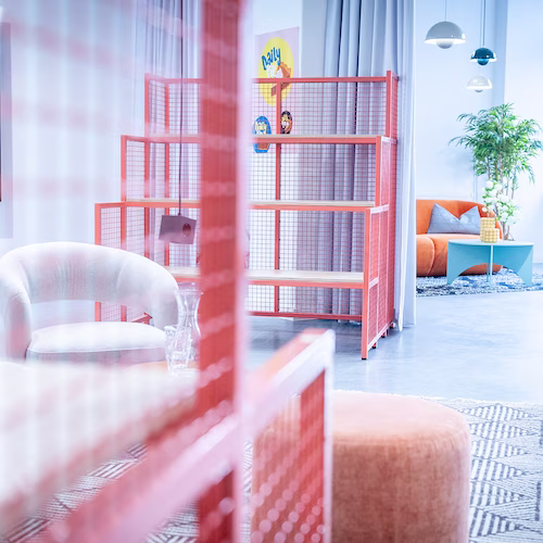 Moderner Wohnraum mit oranger Metallregalwand, weißem Sessel, oranger Couch und Pflanzen.