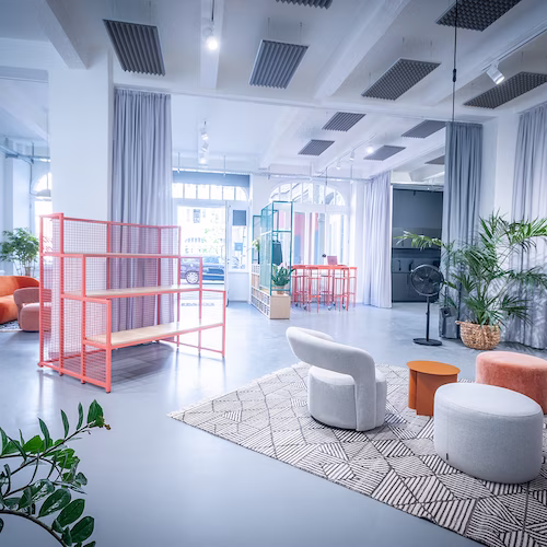 Helles, modernes Wohnzimmer mit weißen Sesseln, pinkem Regal, Teppich und Zimmerpflanzen.