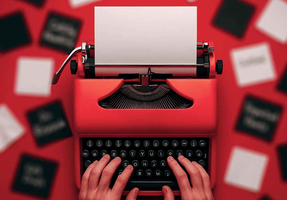 Hands typing on a red vintage typewriter with a blank sheet of paper, surrounded by blurred black and white cards on a red surface.
