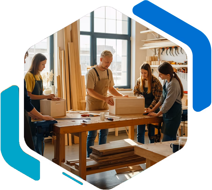Quatre personnes travaillant en atelier de menuiserie sur deux caisses en bois posées sur une grande table de travail.