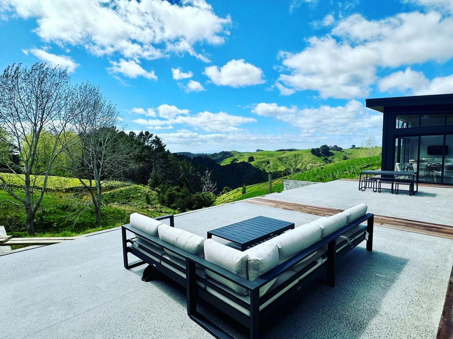 Modern patio furniture overlooks lush green hills under a bright blue sky, creating a tranquil outdoor retreat.