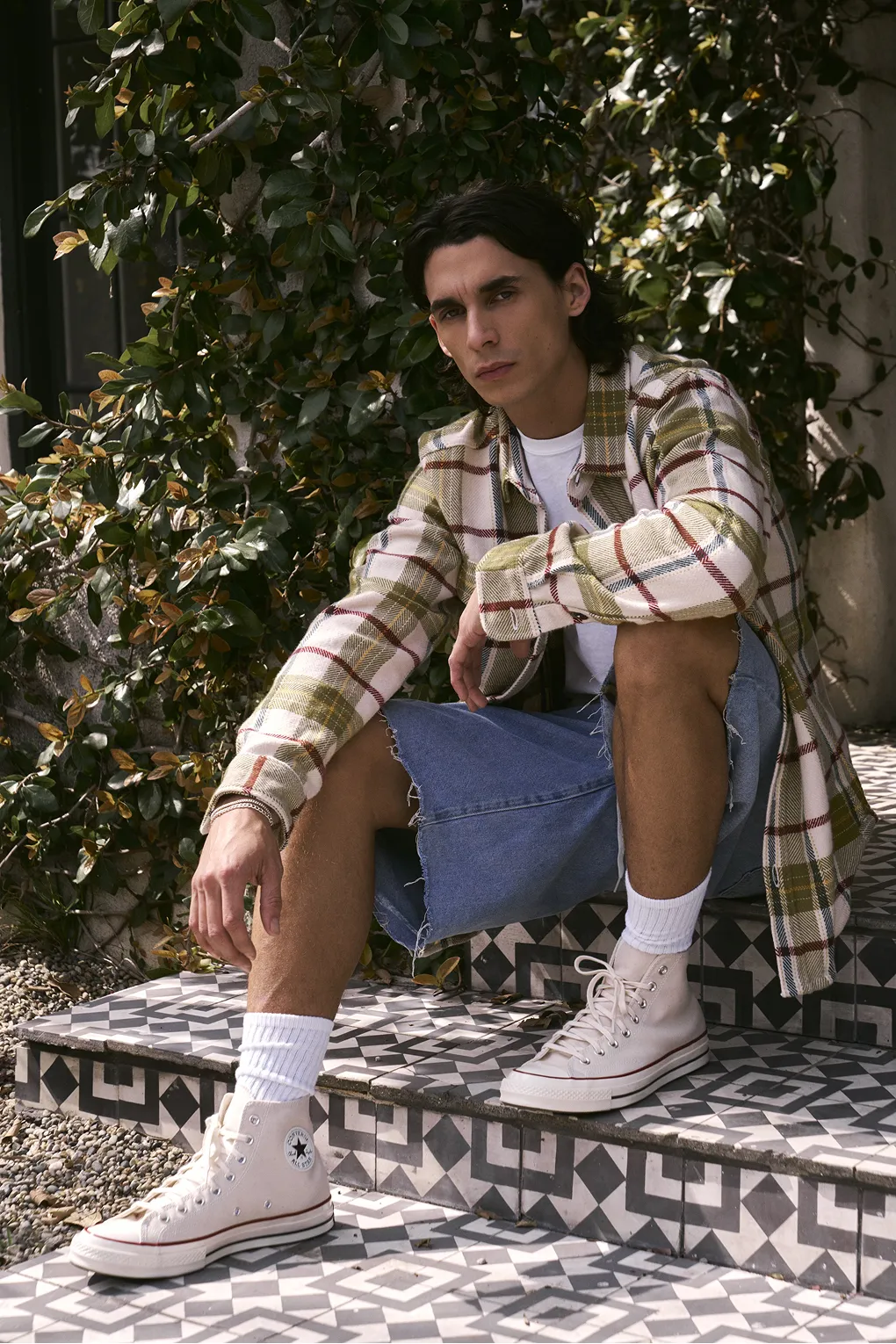 Stylish man in a checked shirt, denim shorts and white converse shoes