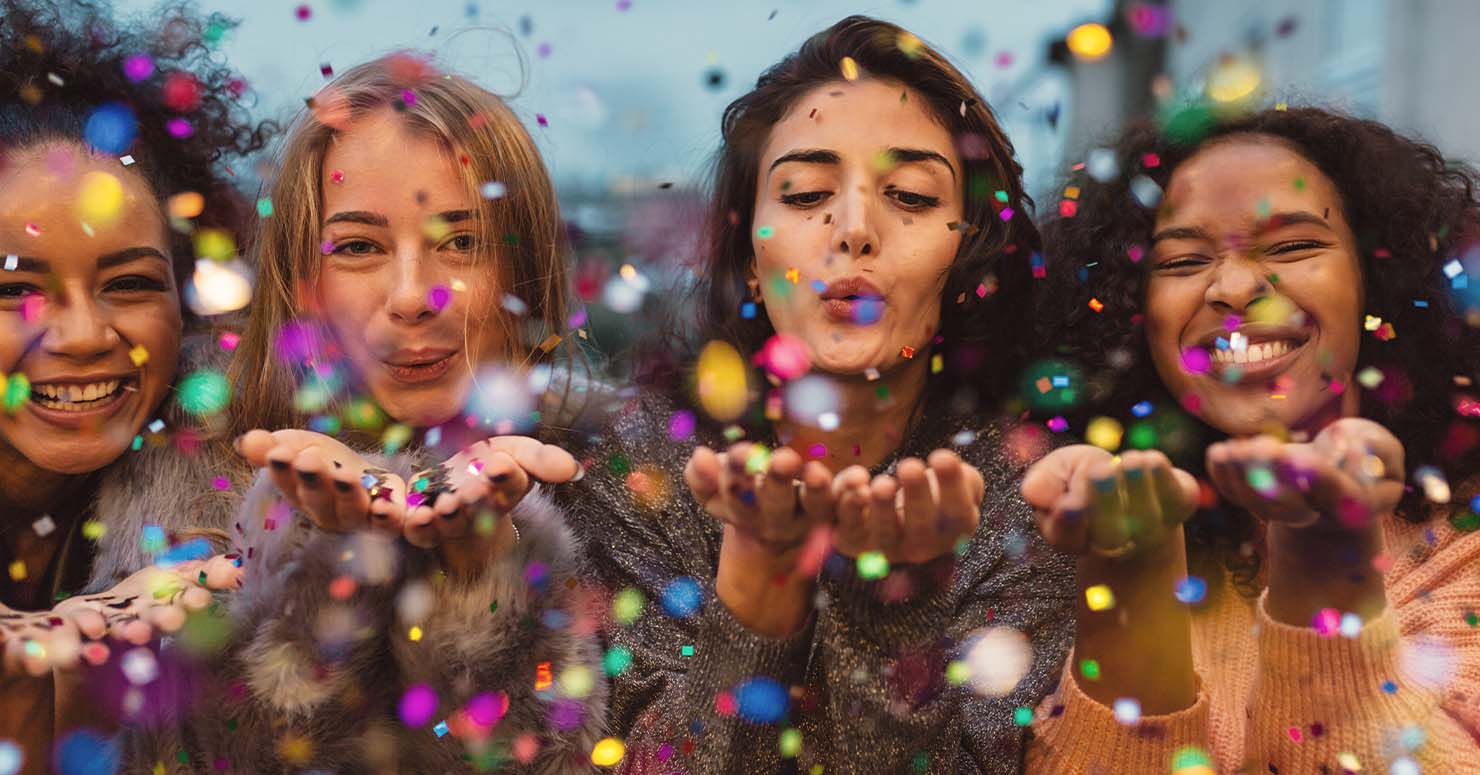 women blowing confetti at camera