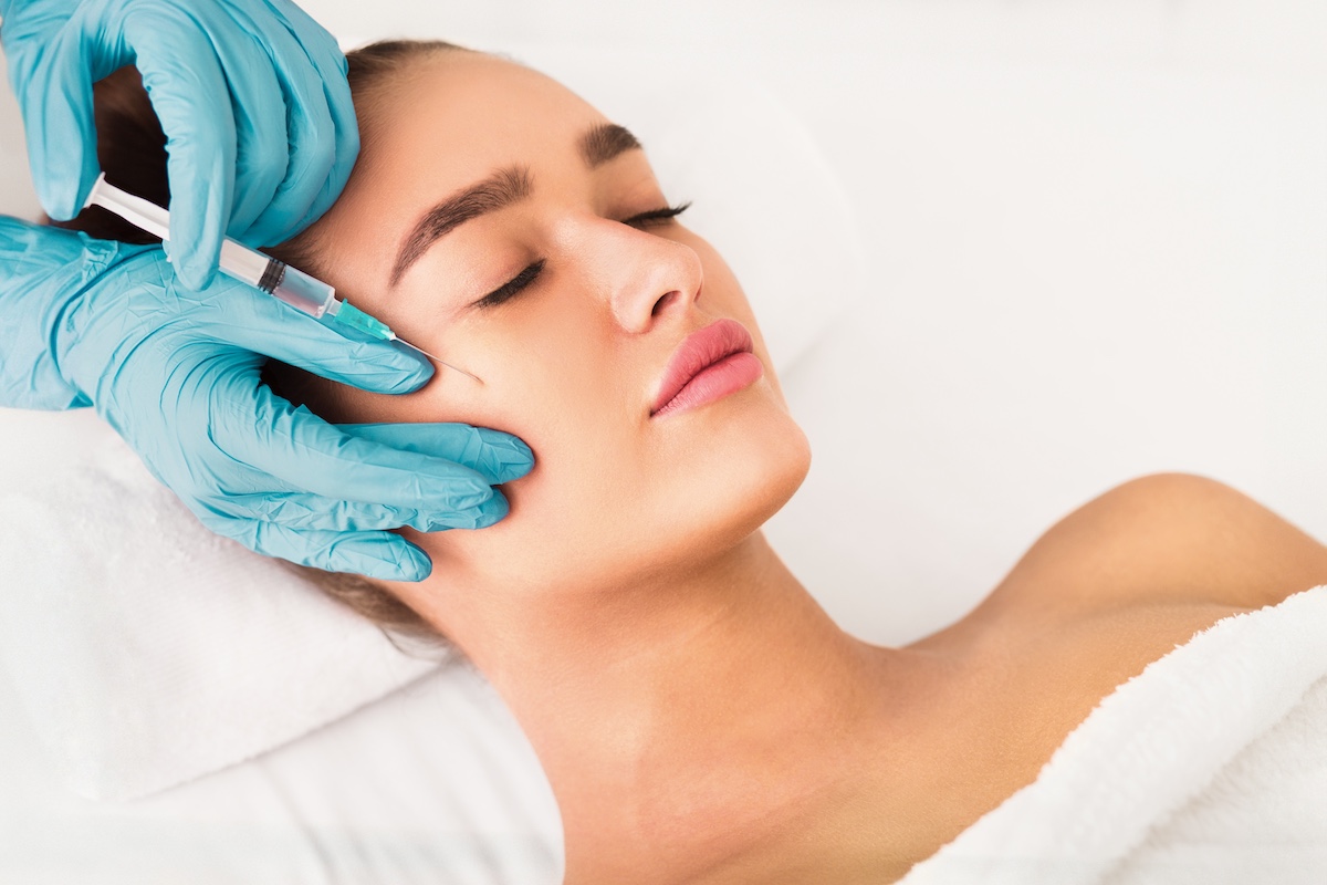 A woman lying down being injected in her cheek.