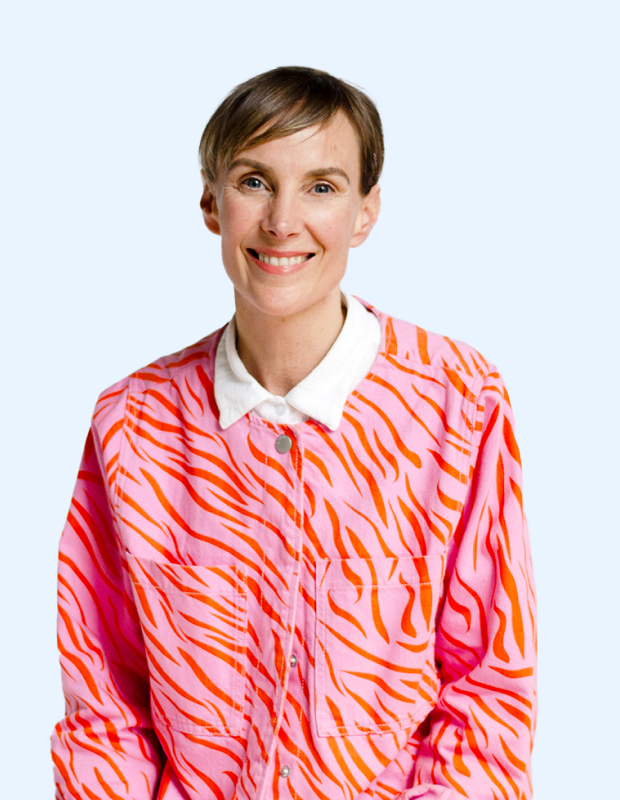 Face on portrait of Charlie Lee, Product Manager at Dot Loves Data. She is smiling at camera, arms are straight down, wearing a light pink denim jacket with red pattern on top, she has a white collared shirt under the jacket. The image is on a light blue background.