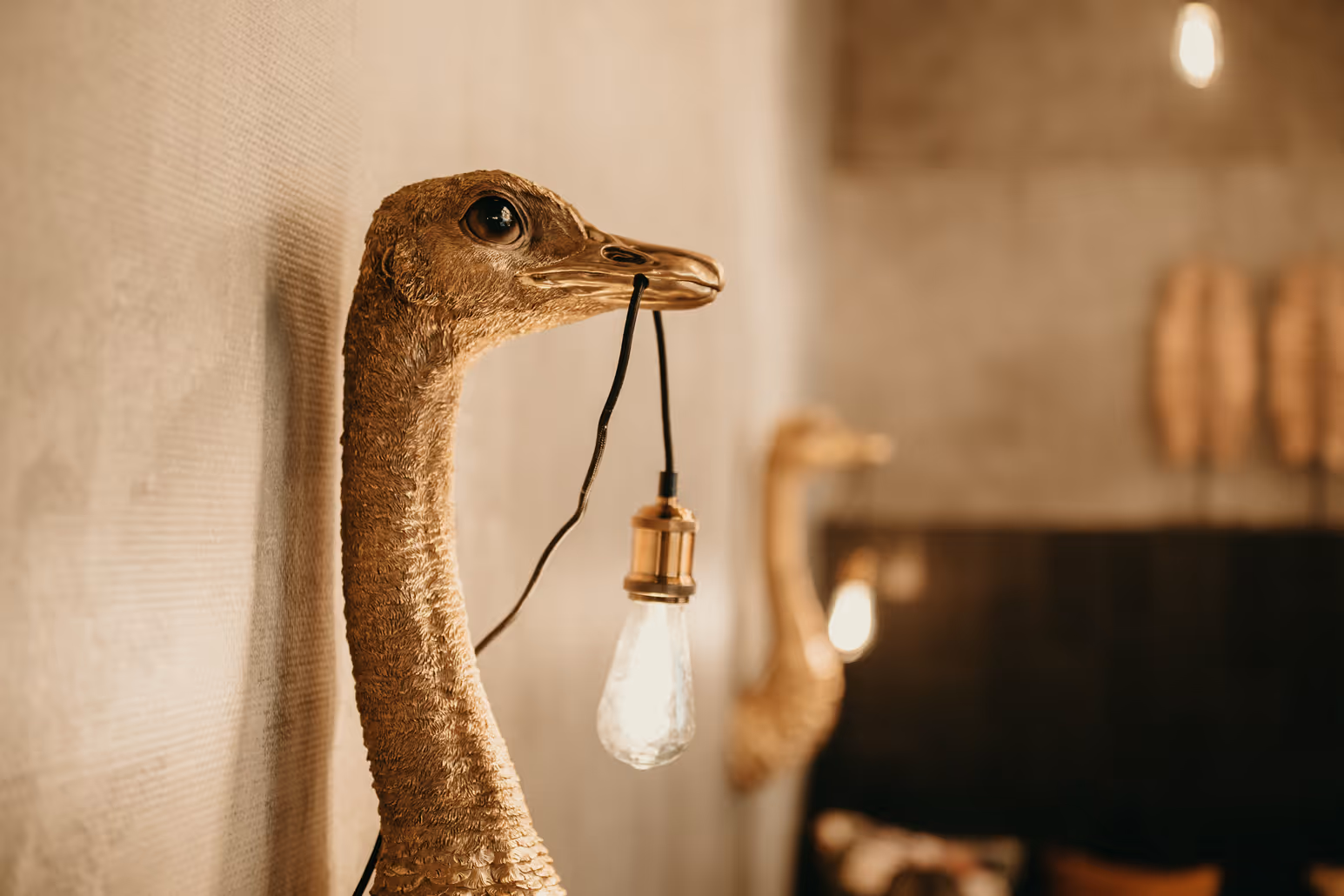 Goldfarbener Schwan-Kopf mit einer Glühbirne, die aus dem Schnabel hängt, an einer Wand montiert.