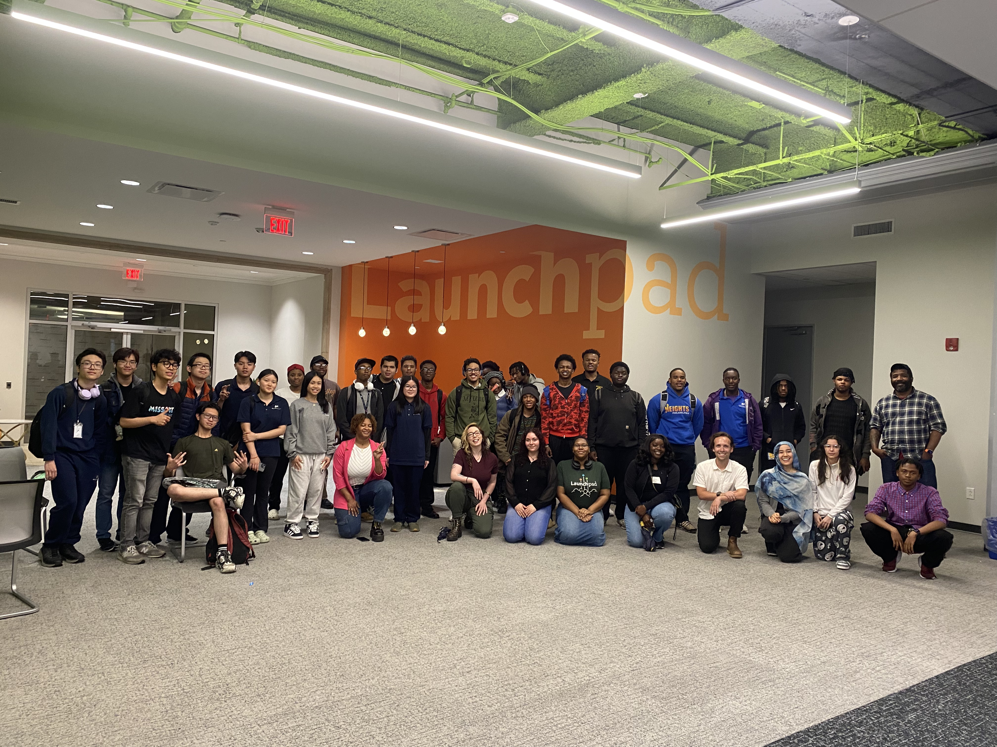 Jamie kneeling and smiling, posing with a group of highschool students and PhillyCHi volunteers at Launchpad offices