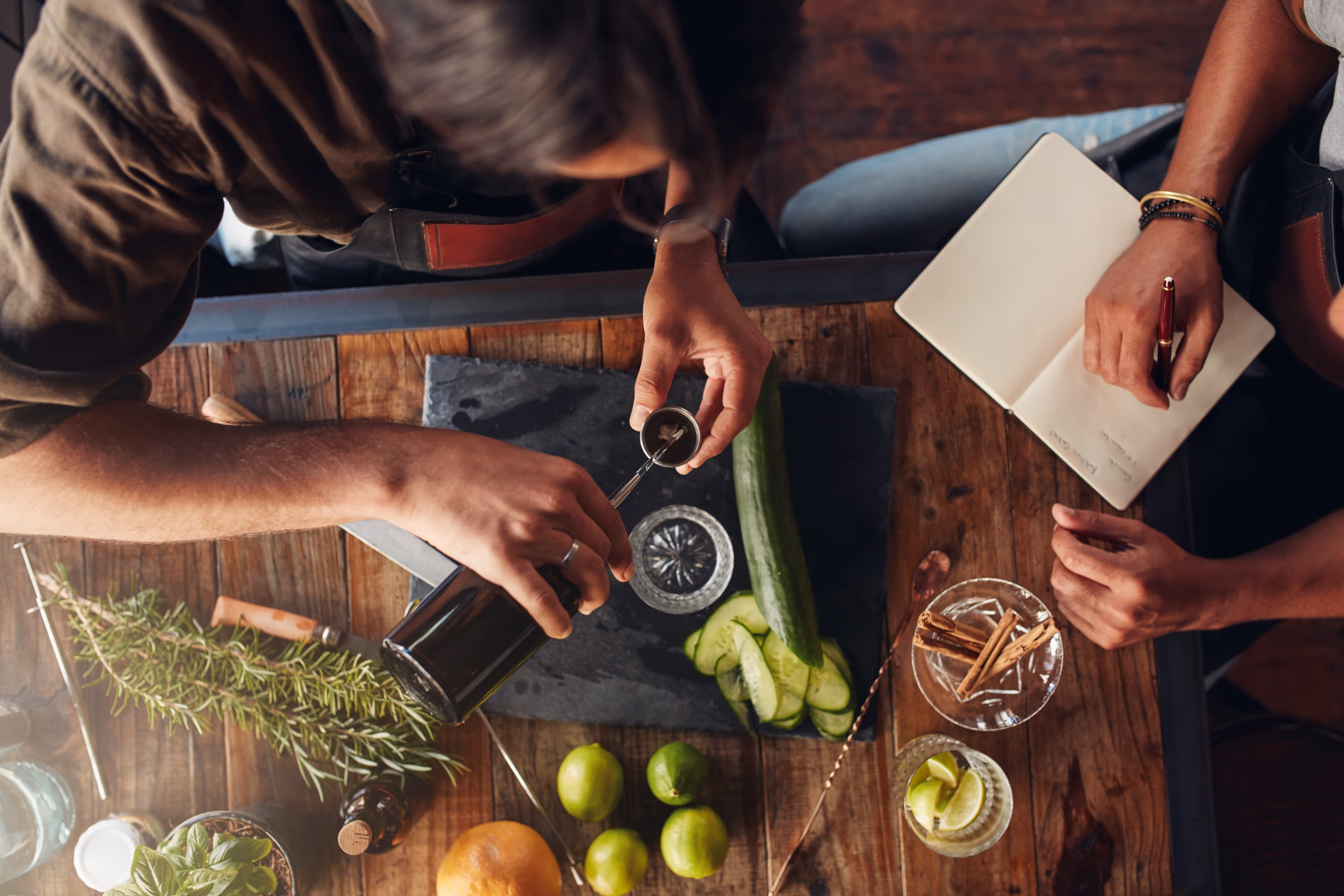 Overhead view of two bartenders creating and documenting a cocktail recipe