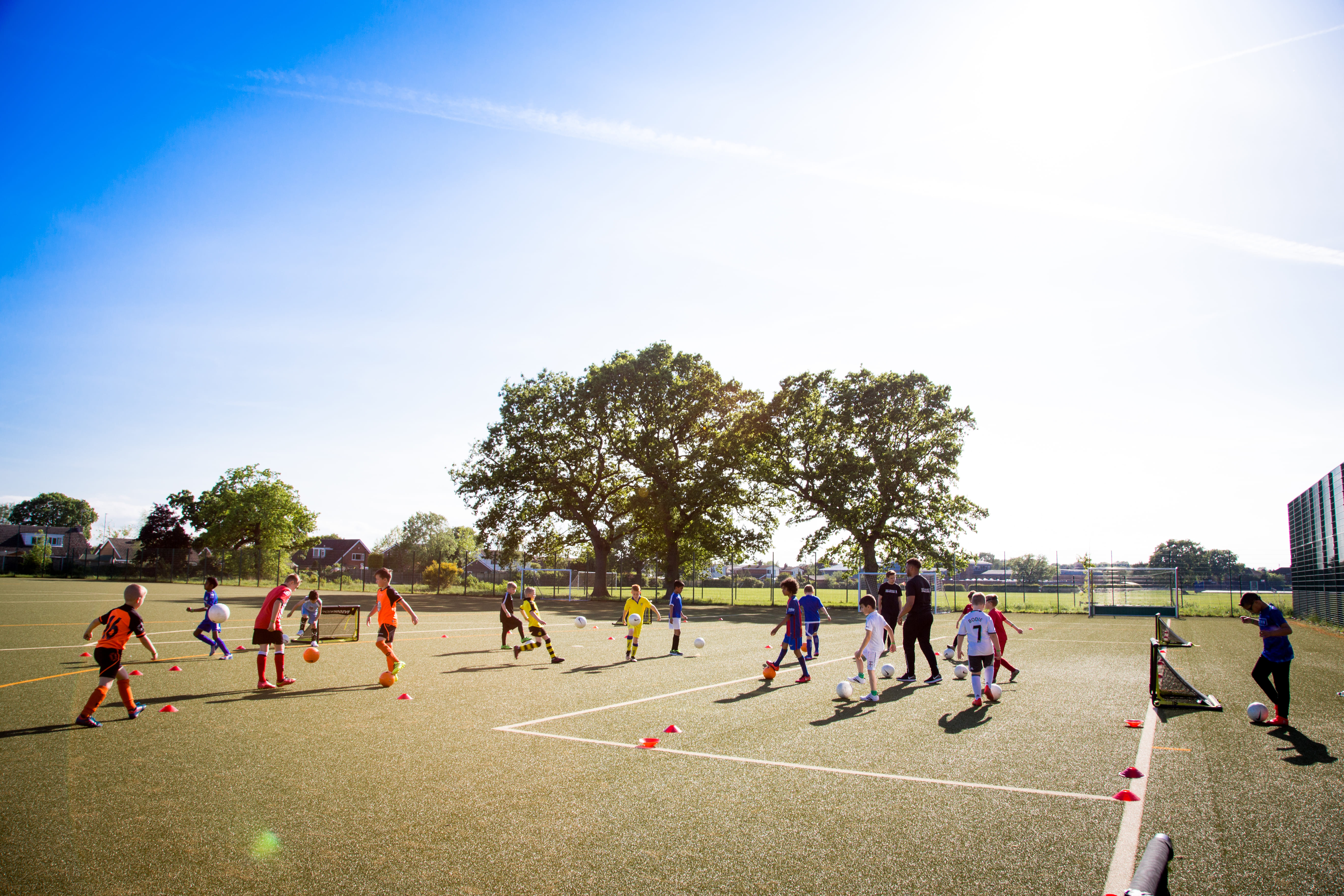 Children playing soccer on a green pitch with clear weather and blue skies.