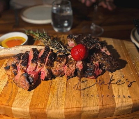 In-house dry-aged prime tomahawk steak sliced and served on custom branded Duke's wooden carving board
