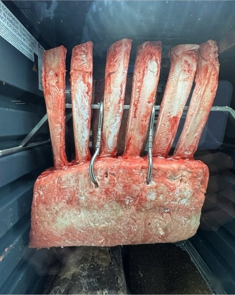 In-house dry-aged prime tomahawk rack hanging in aging locker at Duke's Steakhouse