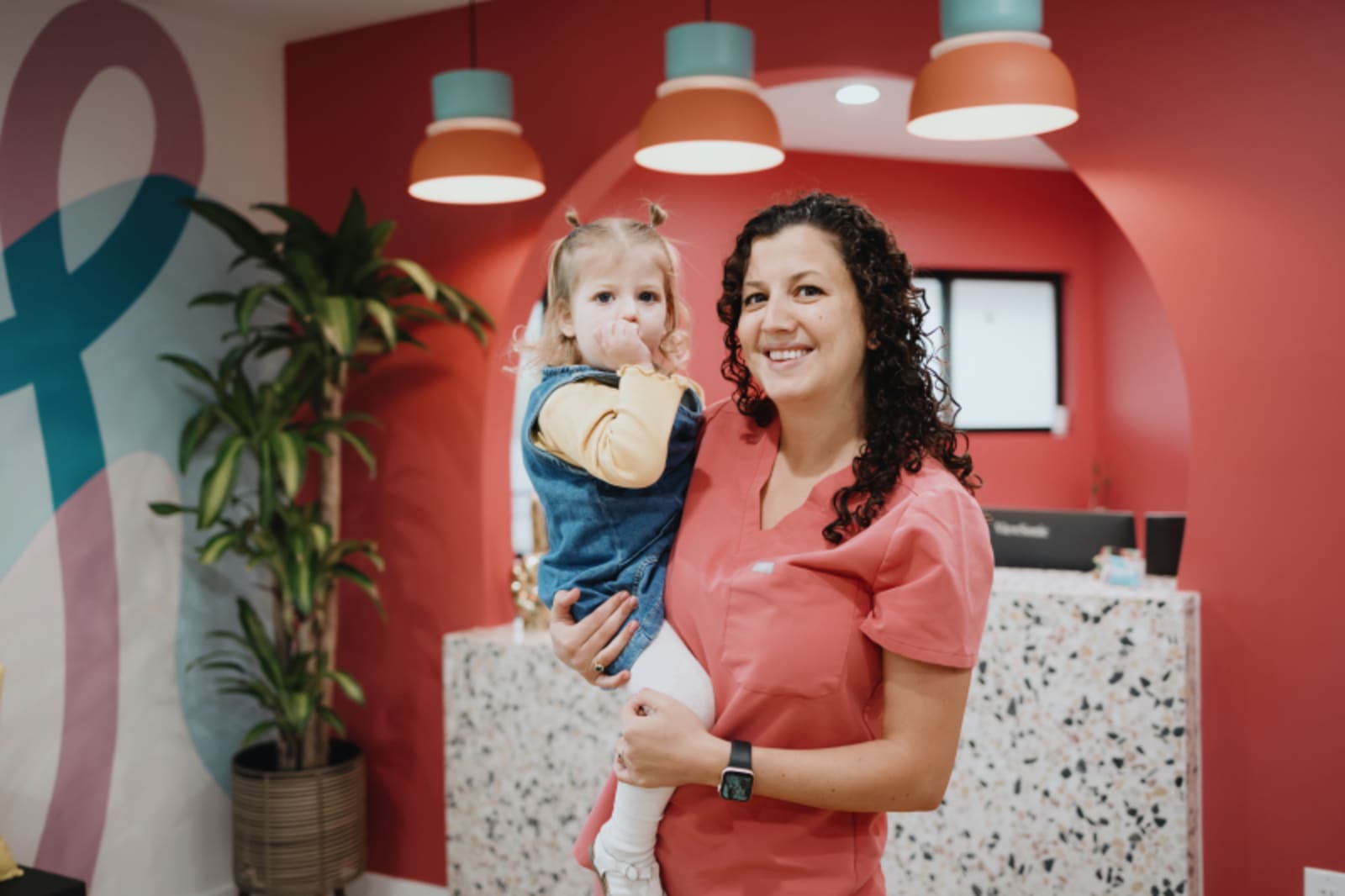Female dentist holding a smiling child in a bright, welcoming office setting