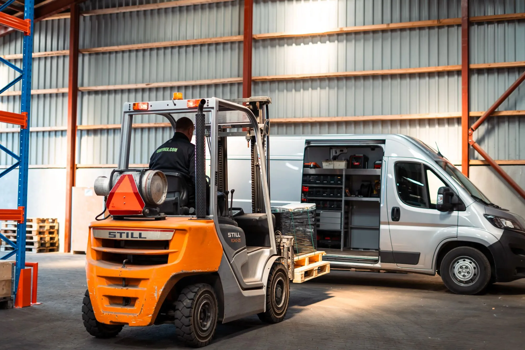 Gaffeltruck med chauffør løfter paller nær en åben varevogn i et lager.