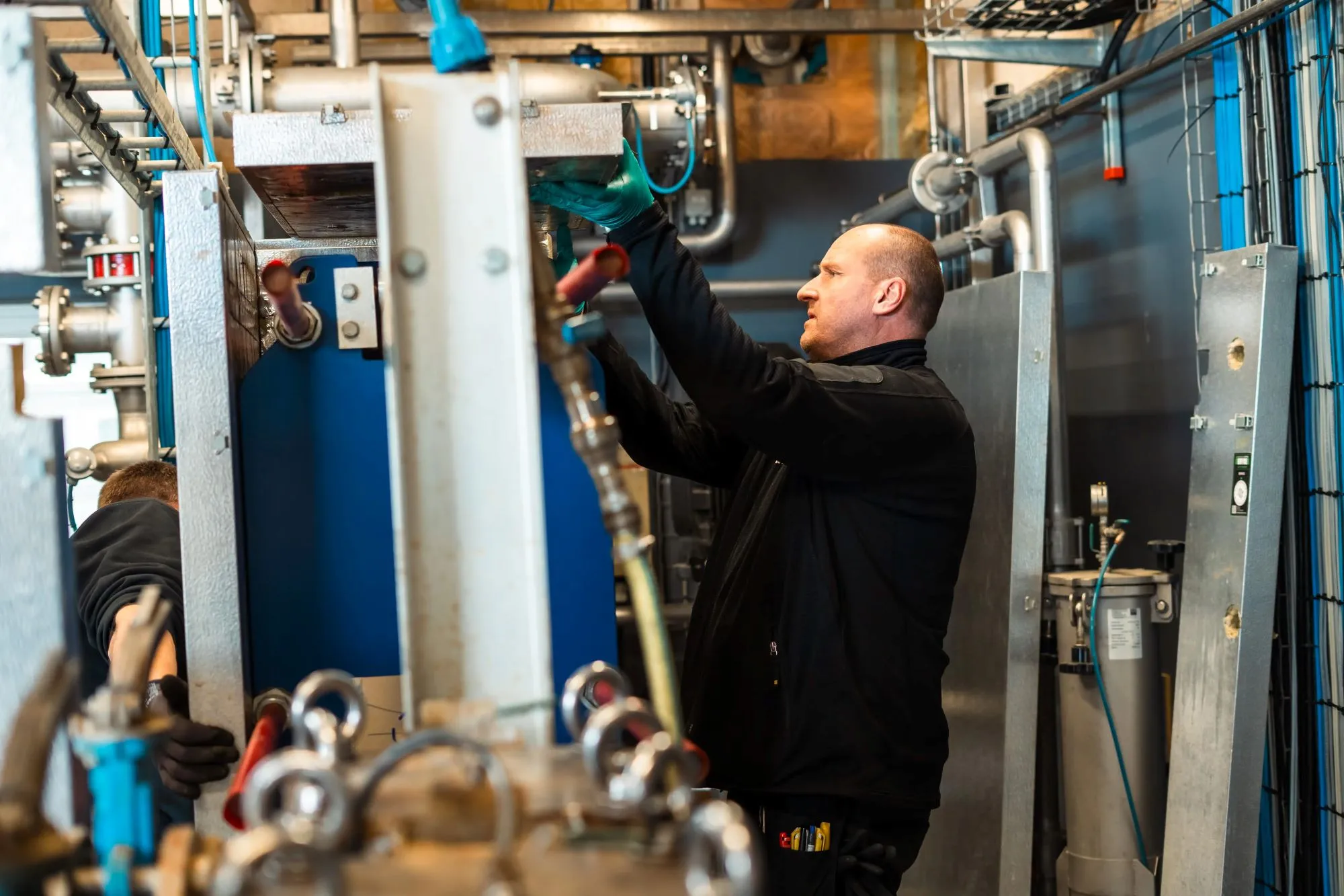 To mænd arbejder med at installere eller reparere teknisk udstyr i et maskinrum.