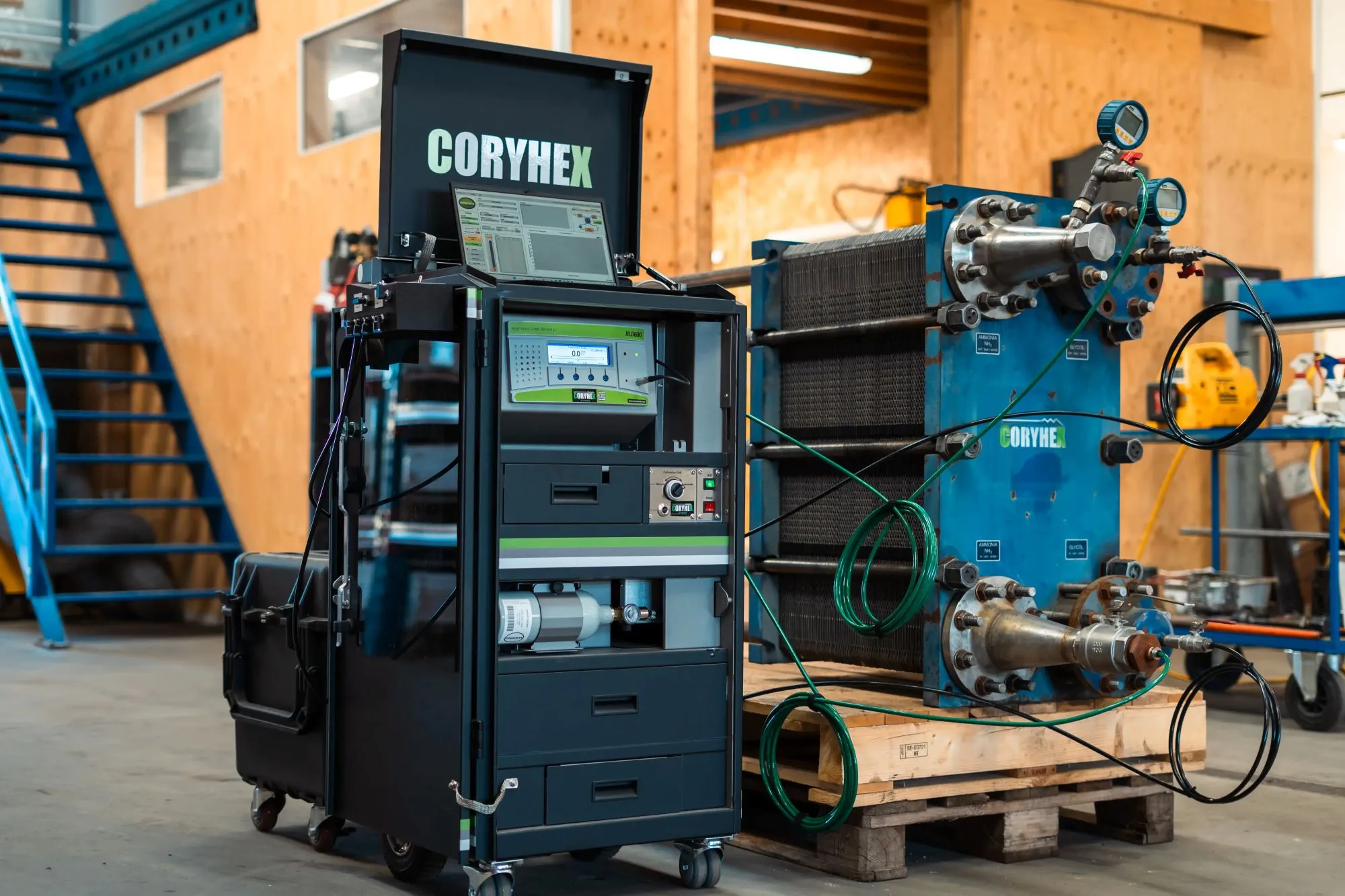Industrielt udstyr med apparatmærket CORYHEX, placeret i et værksted med trævægge og metaltrappe i baggrunden.