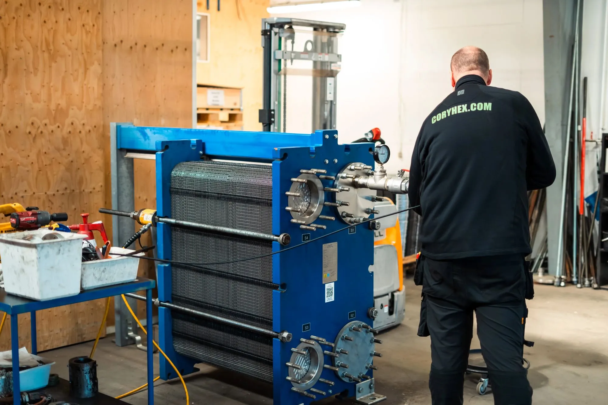 Tekniker arbejder på en stor blå varmeveksler i en industribygning.