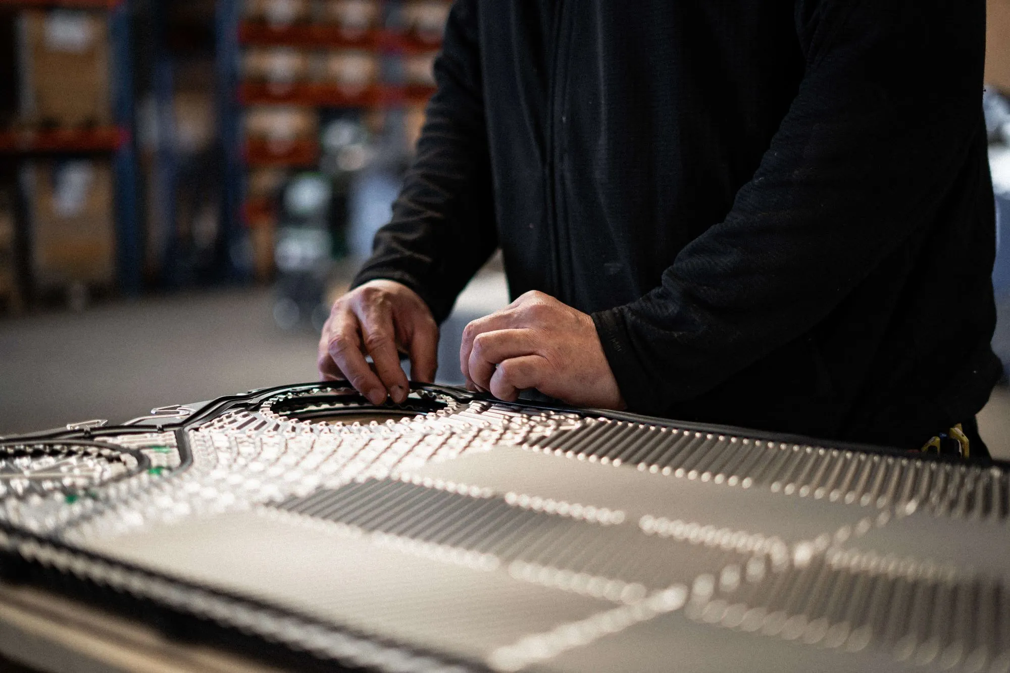 En person iført sort langærmet trøje arbejder med at montere eller justere et komplekst teknisk panel med mange detaljer.