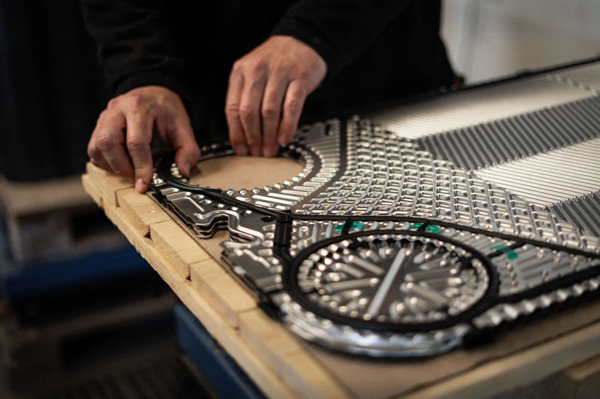 Hænder, der arbejder på et detaljeret metalstykke med komplekse mønstre på et bord.