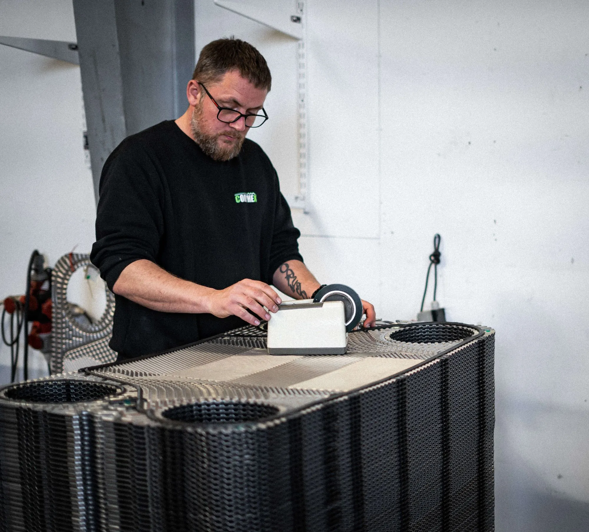 Mand med briller, der arbejder med et stykke industrimateriel i et værksted.