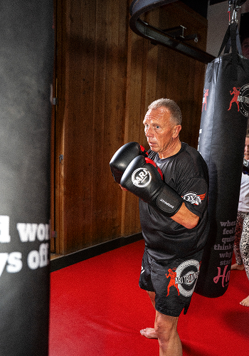 Man in zwarte boksuitrusting oefent boksen in sportschool met bokszak.