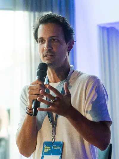 Wilhelm Hammes mit Mikrofon und Veranstaltungsausweis spricht vor Publikum in einem hellen Raum.