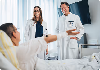 Two doctors smiling and talking with a male patient in a hospital bed.