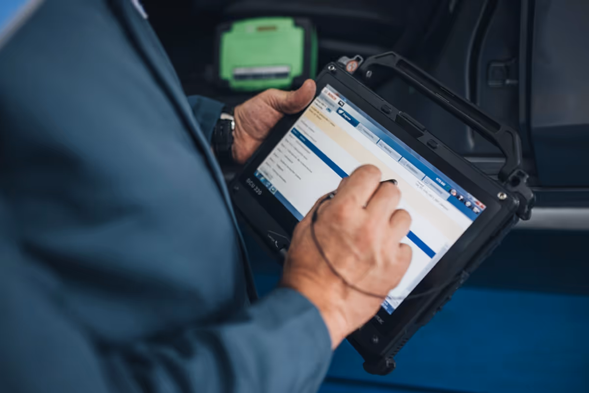 Person using a rugged tablet with a stylus, displaying a list on the screen.