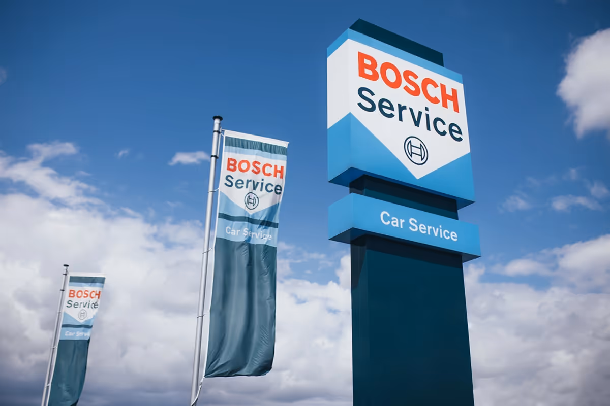 A tall Bosch Service sign and flags indicating car service against a partly cloudy blue sky.