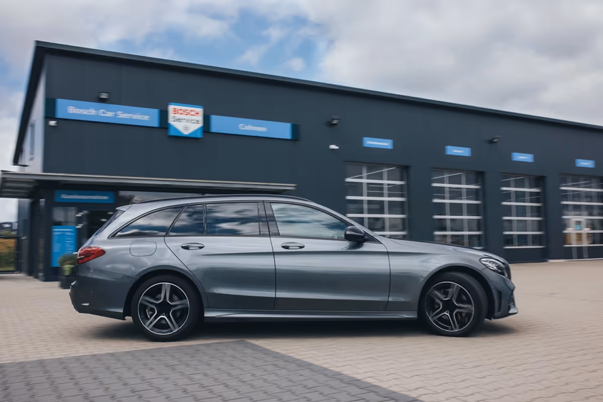 Gray station wagon parked outside a Bosch Car Service garage with closed glass doors.