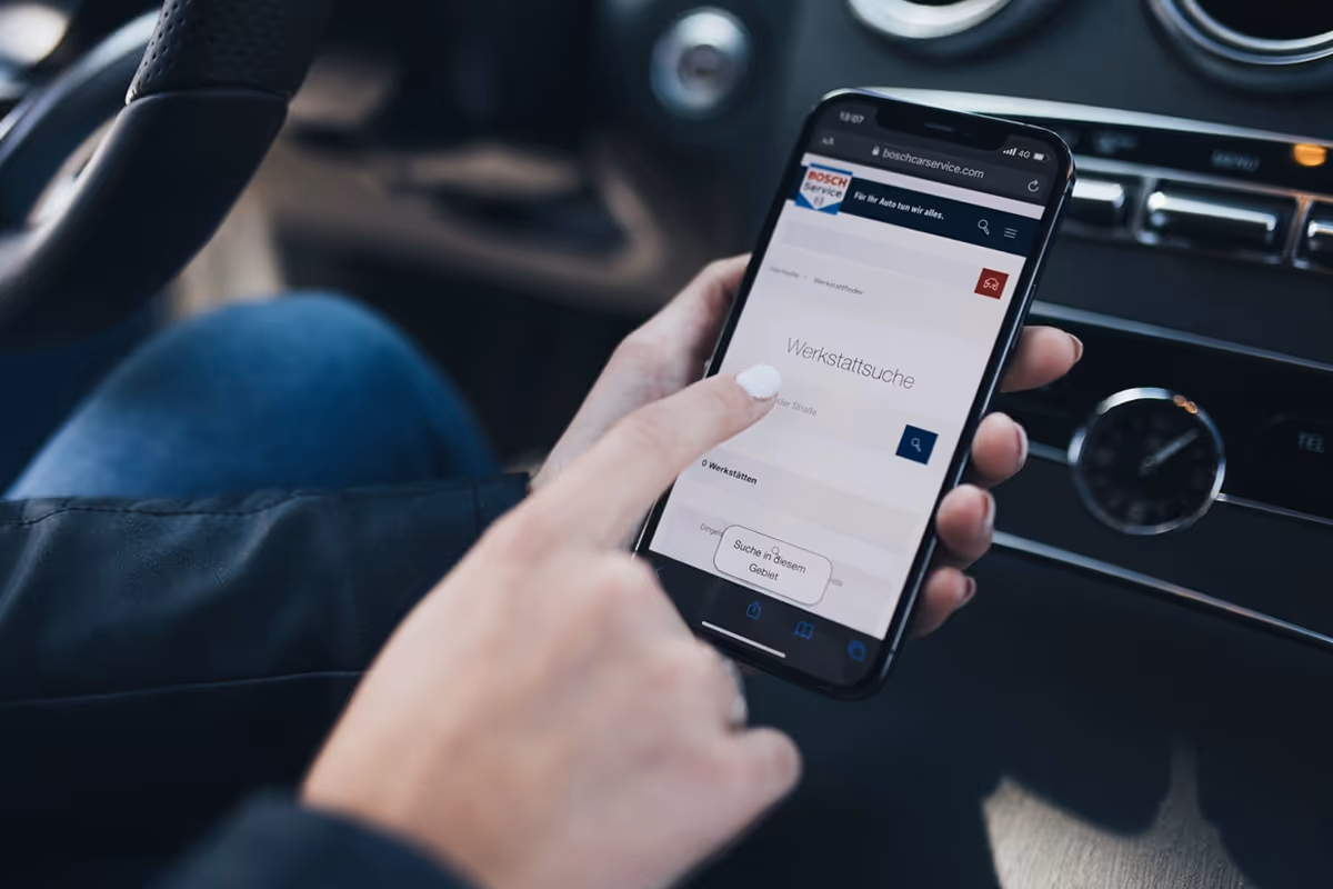 Person using a smartphone inside a car to access a Bosch Car Service website for workshop search.