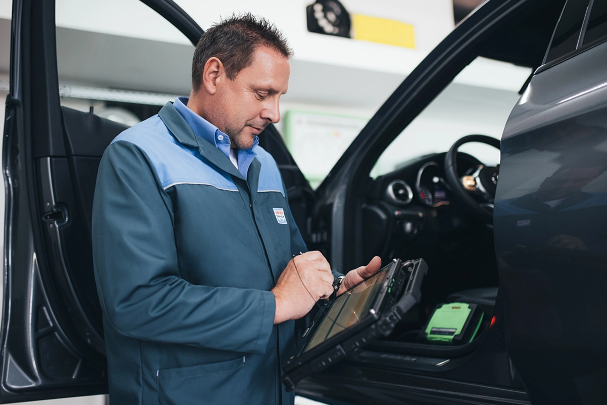 Mechanic in a blue uniform using a digital tablet while standing beside an open car door.