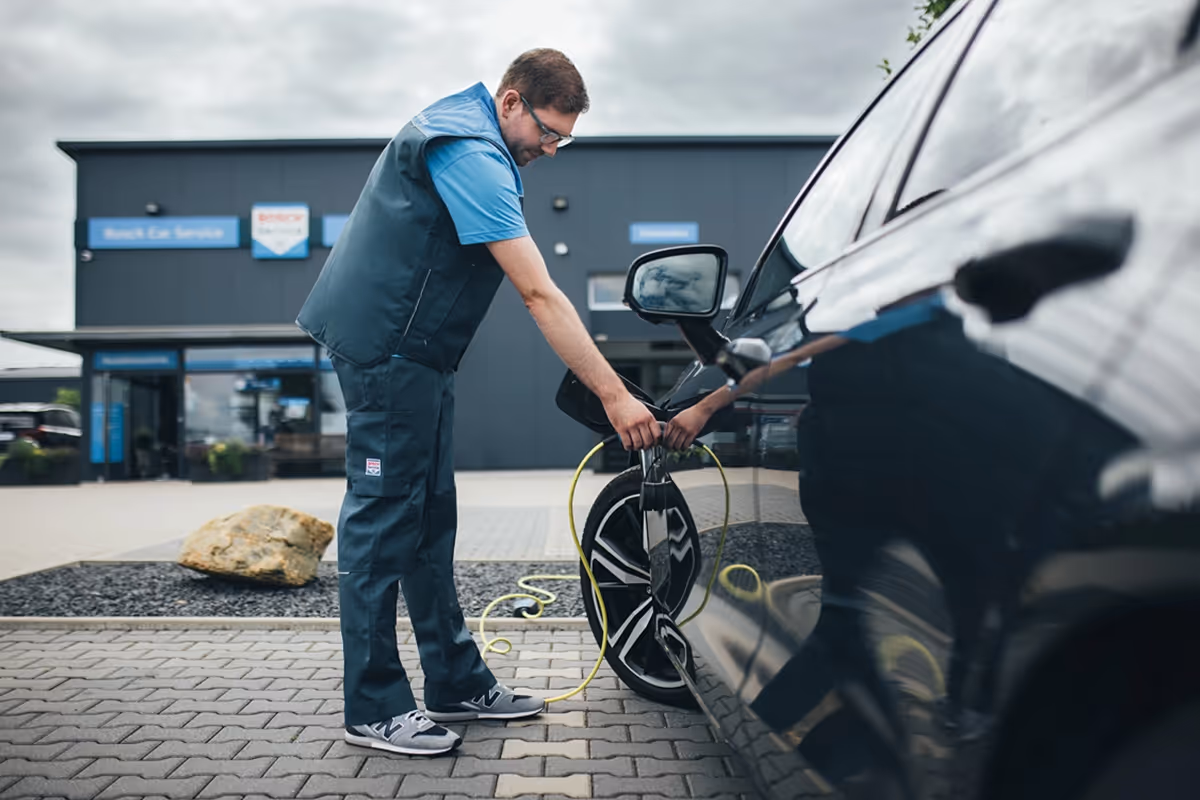 Man plugging in an electric car to a charging station outside a modern service building.