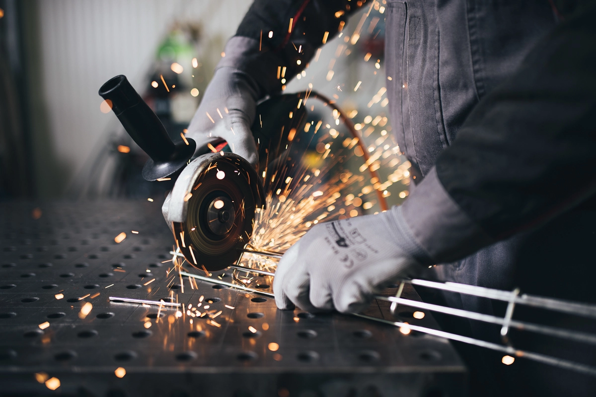 Person wearing gloves using an angle grinder to cut metal rods with sparks flying.