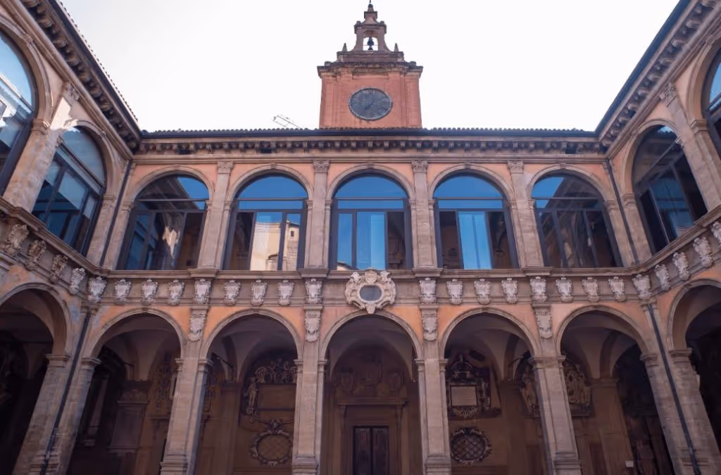 Historic courtyard with arched colonnades on two levels and a central clock tower in a brick building.